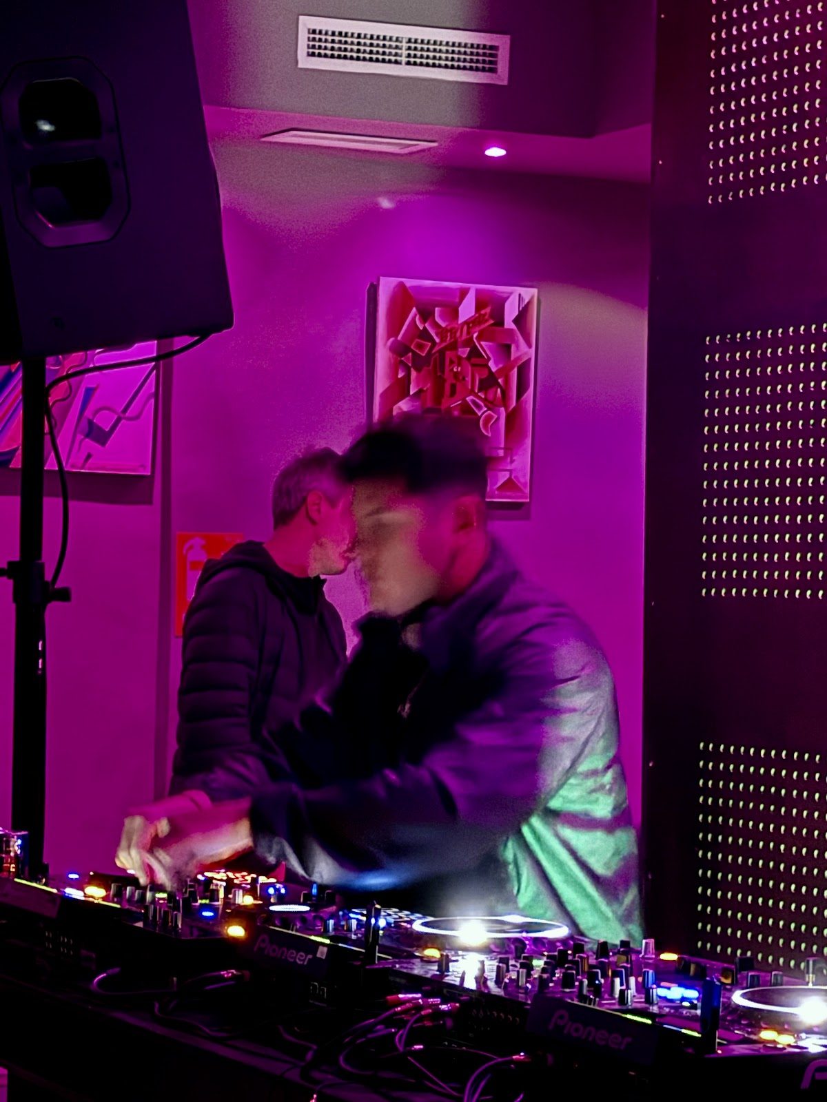 Un DJ pincha música en el 11 Art Club, con una iluminación colorida y arte abstracto de fondo.