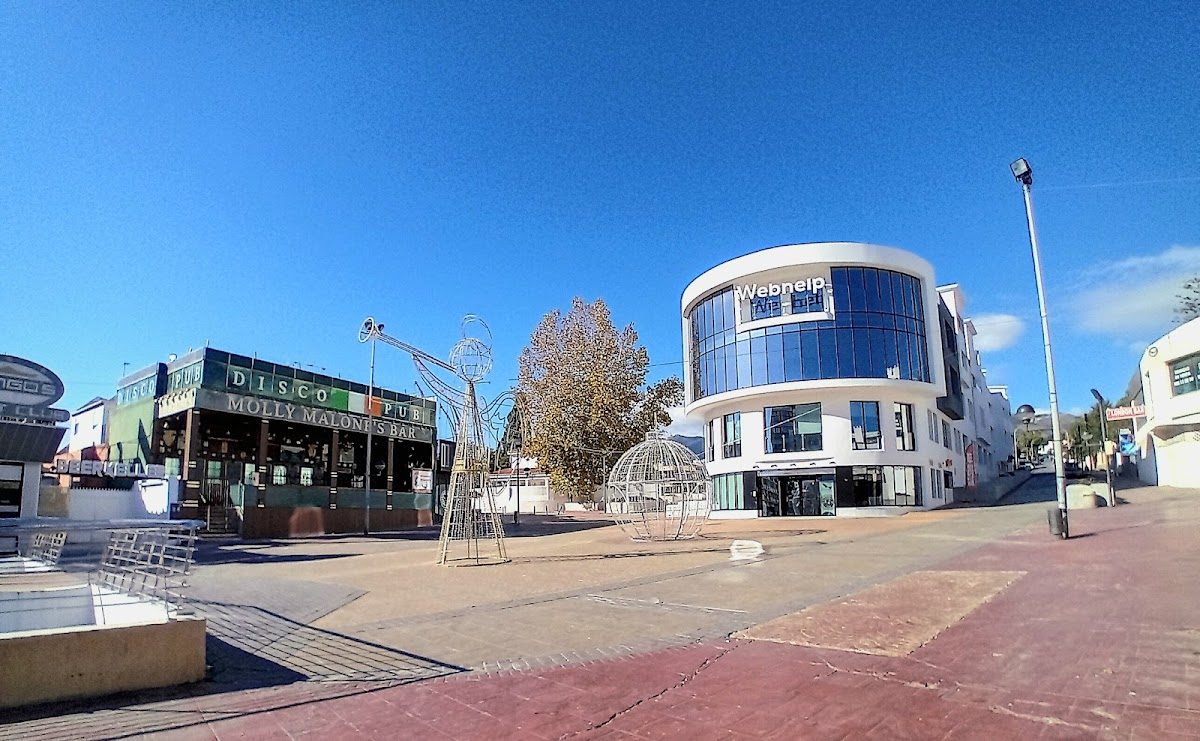 24 Hour Square features modern buildings and a disco, with outdoor seating and sculptures in a sunny plaza.