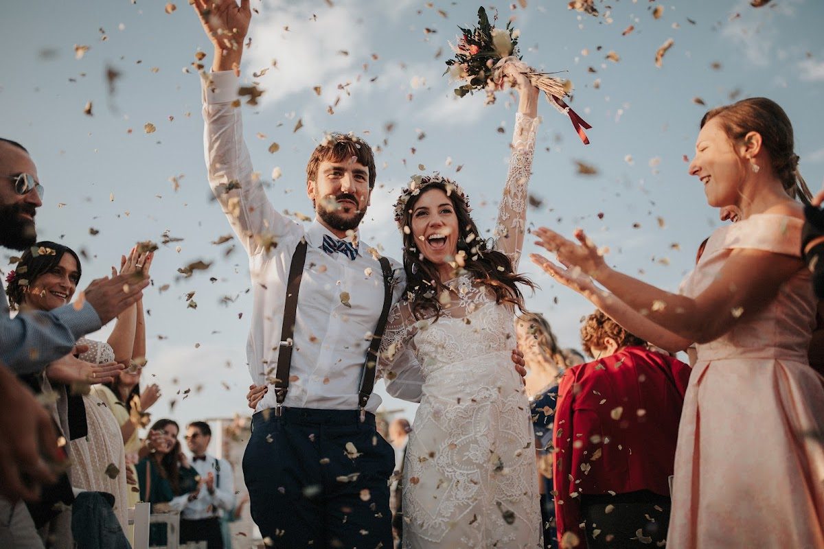 Una pareja feliz celebra su boda, rodeada de invitados que lanzan confeti.