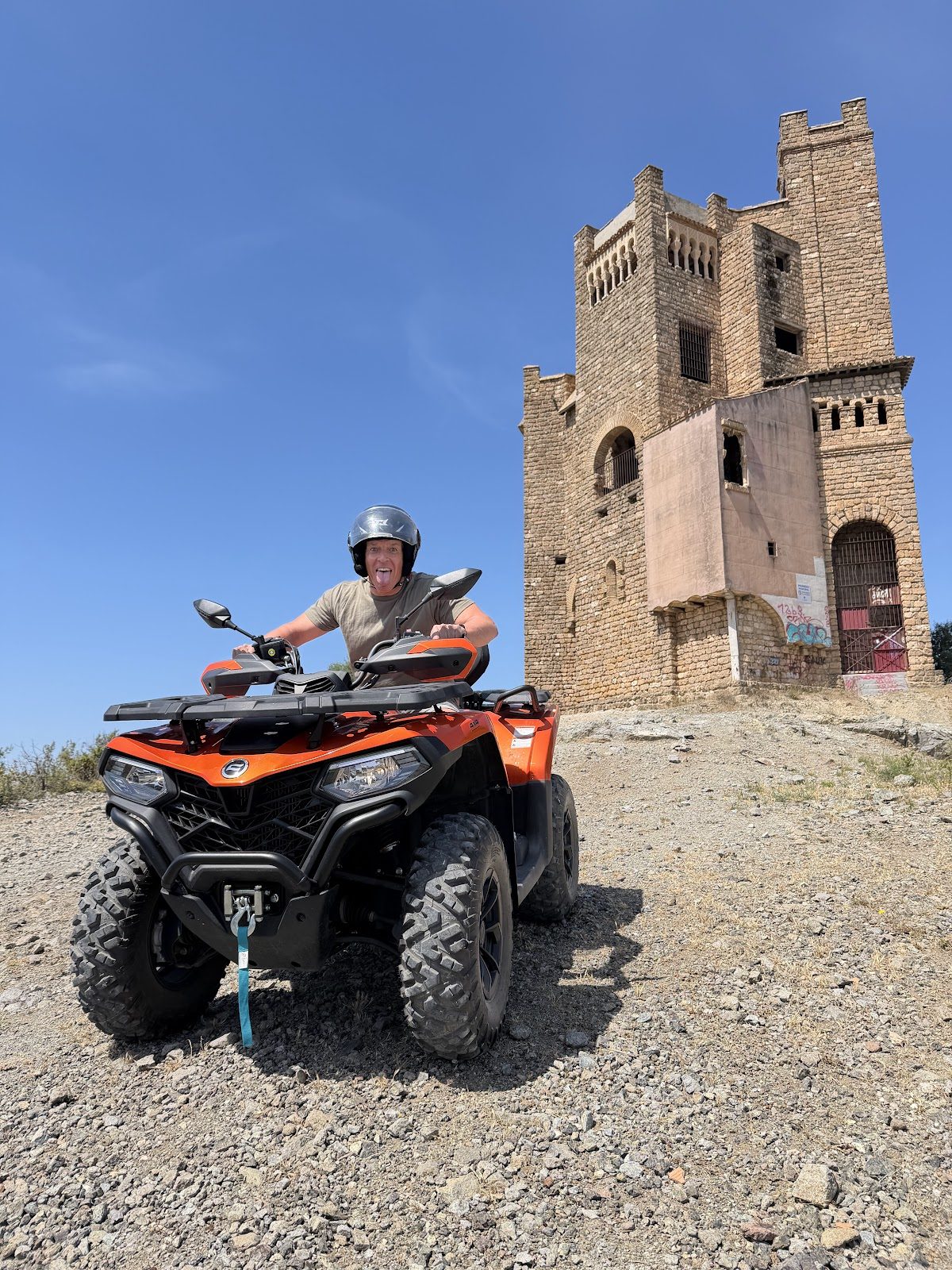 A person on an orange quad bike near a historic stone tower under a clear blue sky.