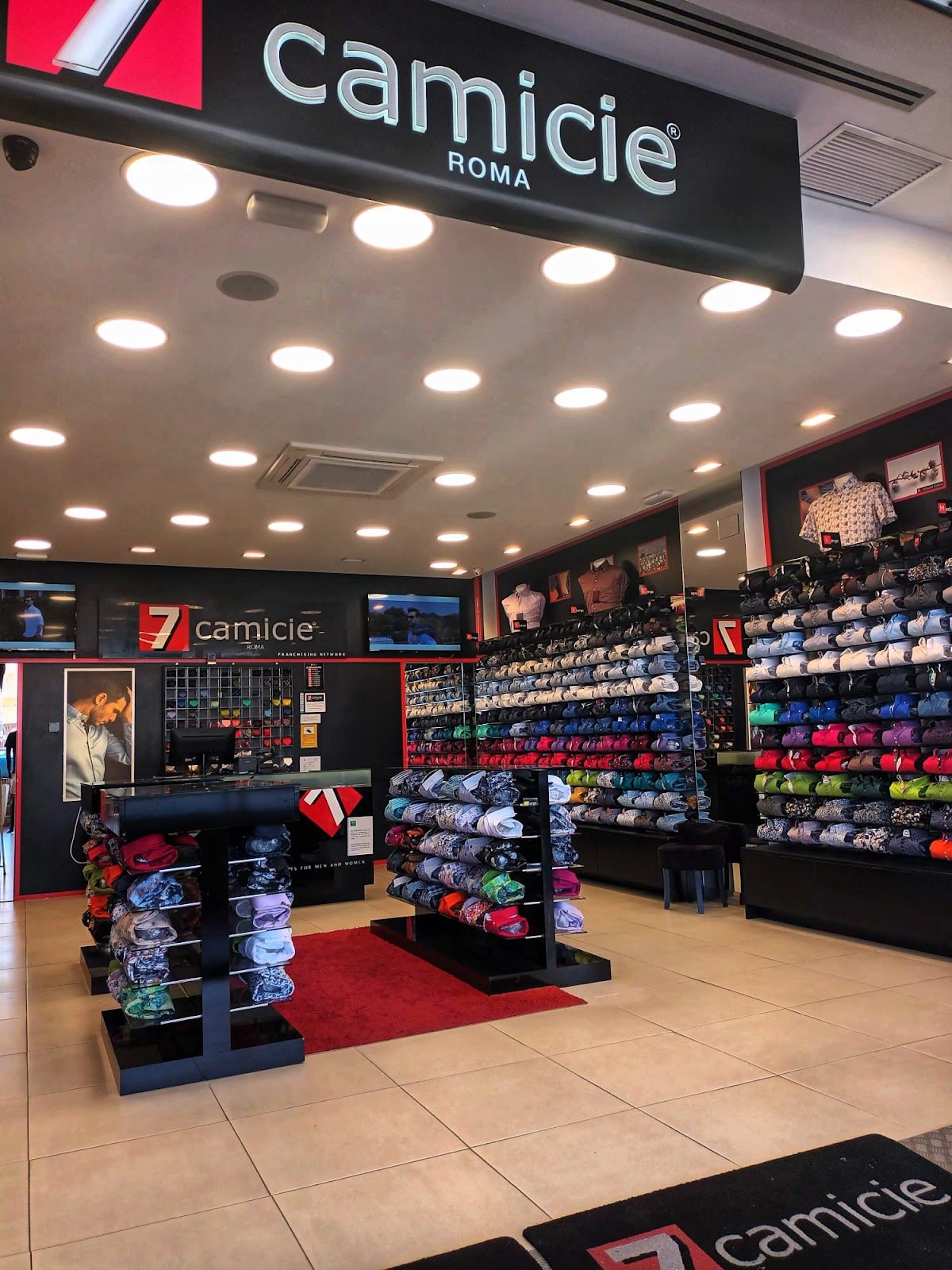 El interior de 7camicie Puerto Marina muestra camisas cuidadosamente dispuestas en percheros y un ambiente comercial moderno.