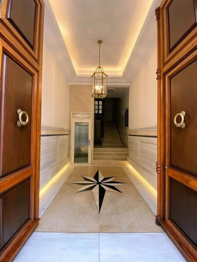 The entrance of A | AGUILERA features elegant wooden doors, a decorative floor with a star design, and an elevator.