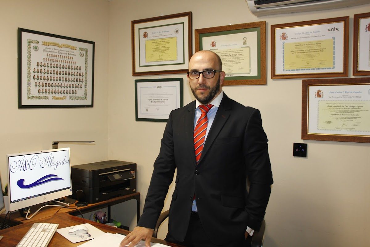 A&O Abogados office featuring a desk, printer, and framed certificates on the wall with a professional in a suit.