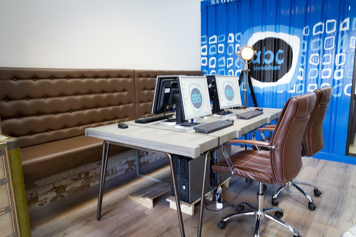 Modern office space at ABC Inmobiliaria with computers, leather chairs, and a blue accent wall.