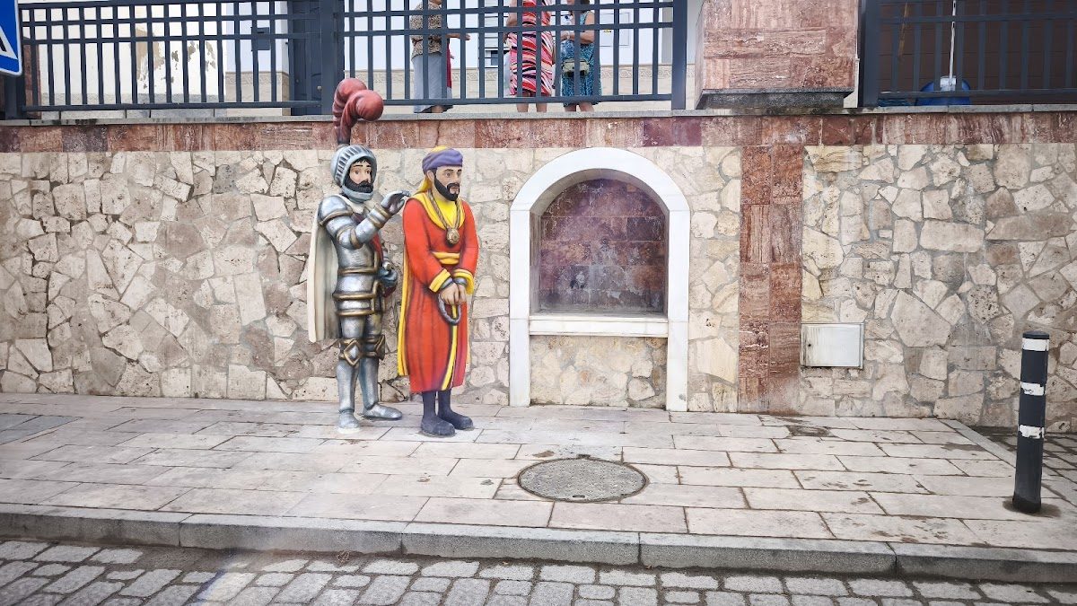 A mural depicting a knight and a captive figure on a stone wall in Cártama.