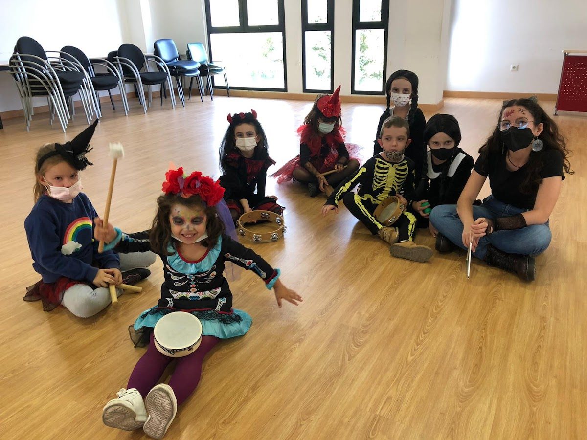 En AC Vive la Música, niños disfrazados tocan instrumentos musicales en una sala luminosa y espaciosa.