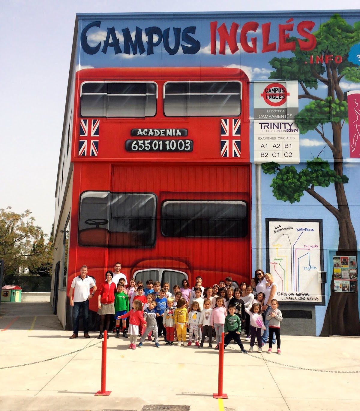 Un grupo de niños y personal posan frente al colorido mural del Campus Inglés que representa un autobús rojo de dos pisos.