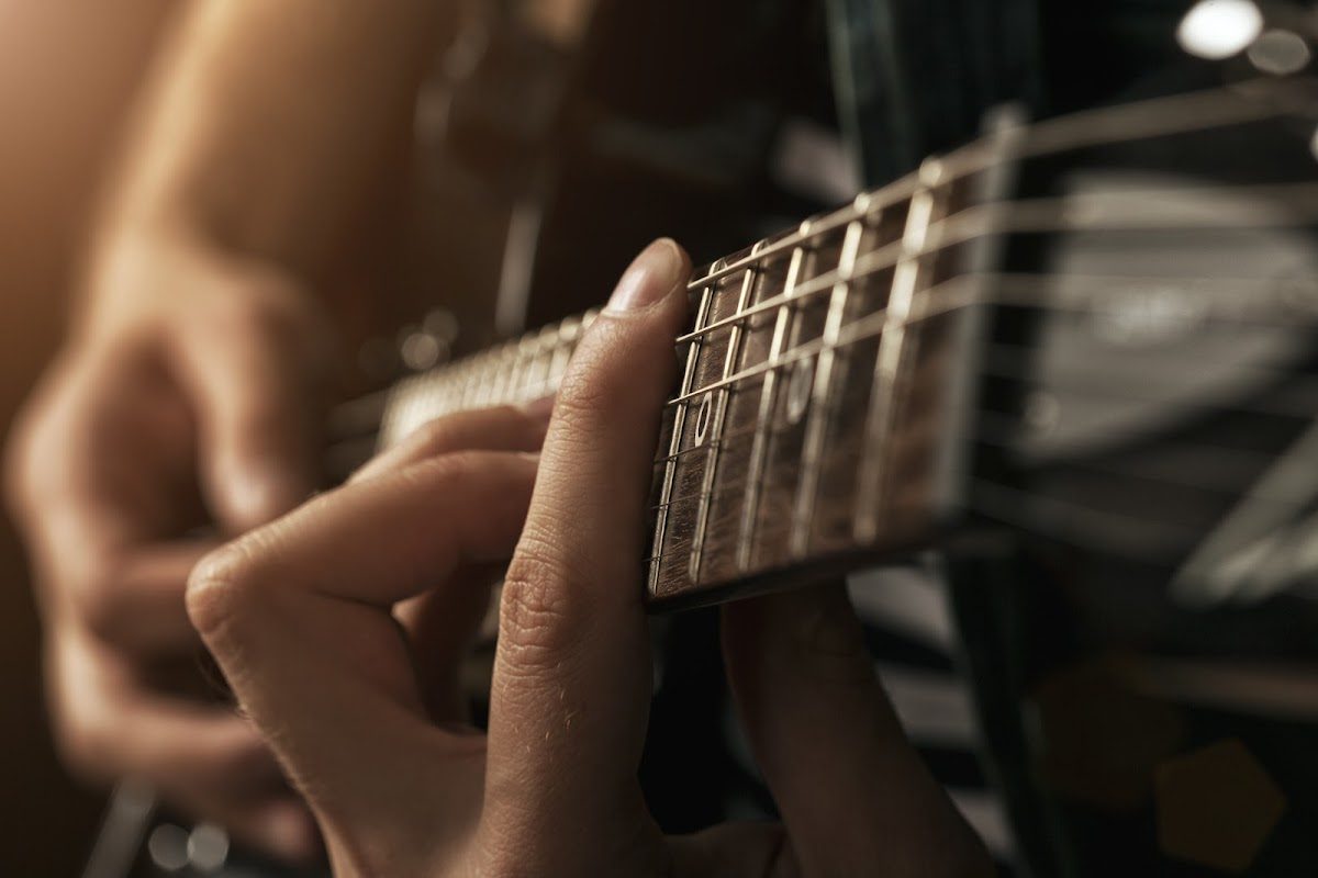 A close-up of hands playing guitar, highlighting finger placement on the fretboard.