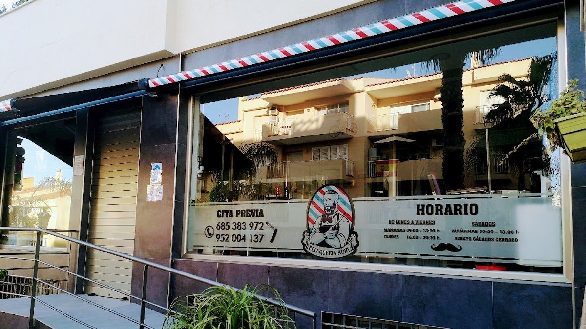 Vista exterior de Adri Peluquería Adry con un poste de barbero y el horario comercial exhibido en la ventana.