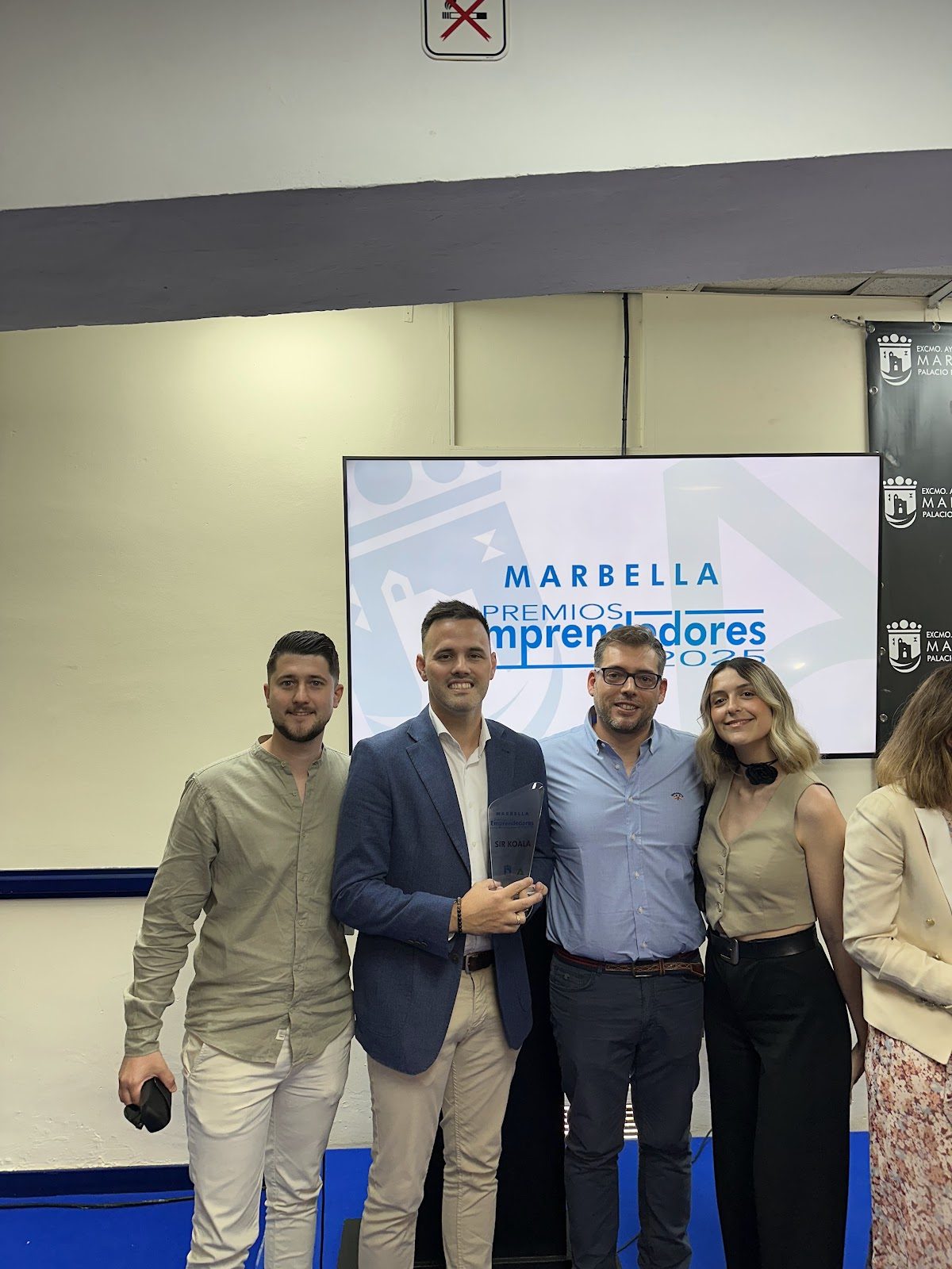 Un grupo de cuatro profesionales posa junto a una pantalla de presentación en un evento, sosteniendo un premio.