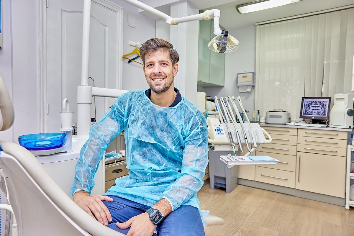 Un dentista con bata quirúrgica azul está sentado en una moderna consulta dental en Alameda Dental.