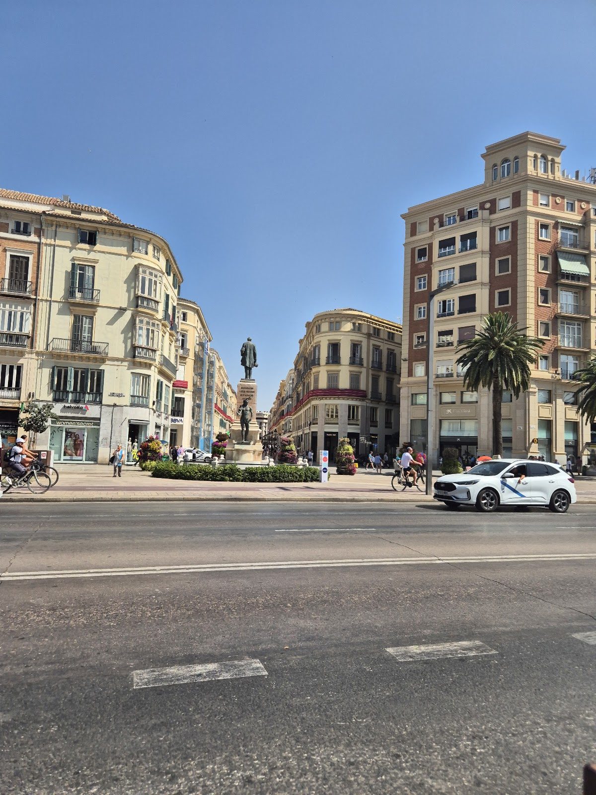 View of Alameda Principal with palm trees, buildings, and a statue in the center of Málaga.