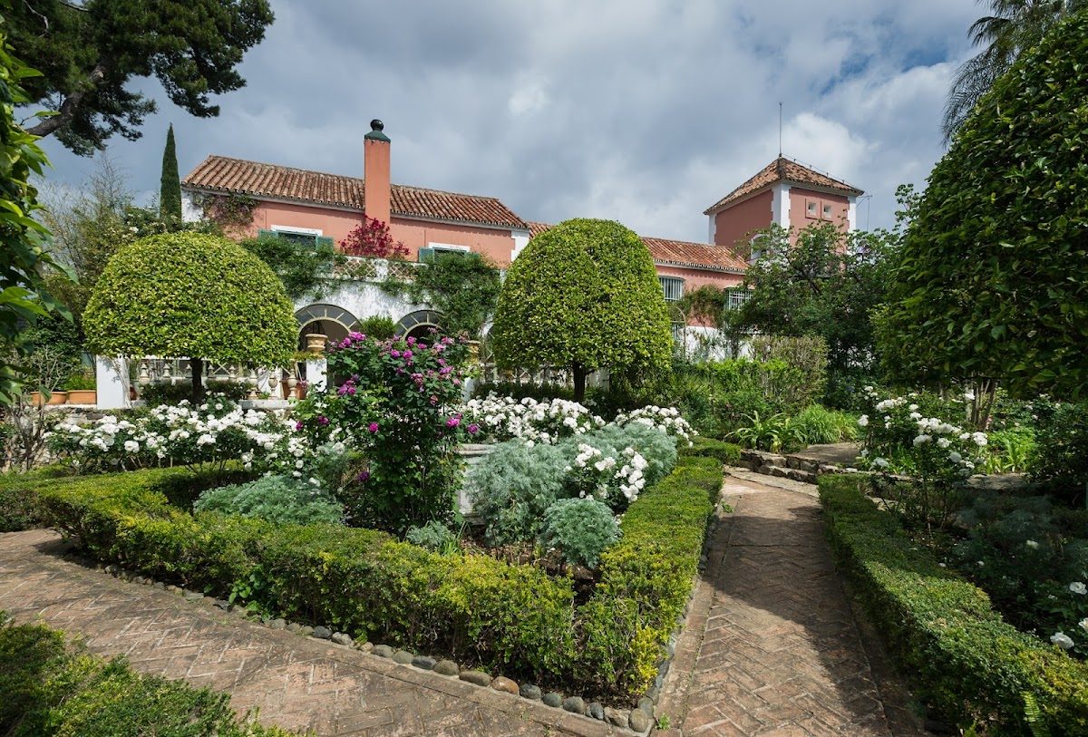 El Alcuzcuz Boutique Hotel cuenta con un exuberante jardín con setos cuidadosamente recortados y flores en plena floración, todo ello enmarcado por un edificio encantador.