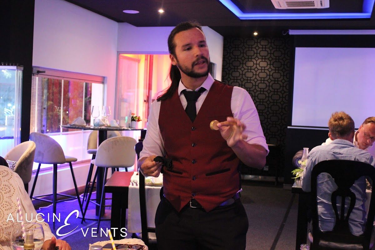 Un hombre con chaleco conversa con los invitados en un elegante espacio para eventos con decoración moderna.