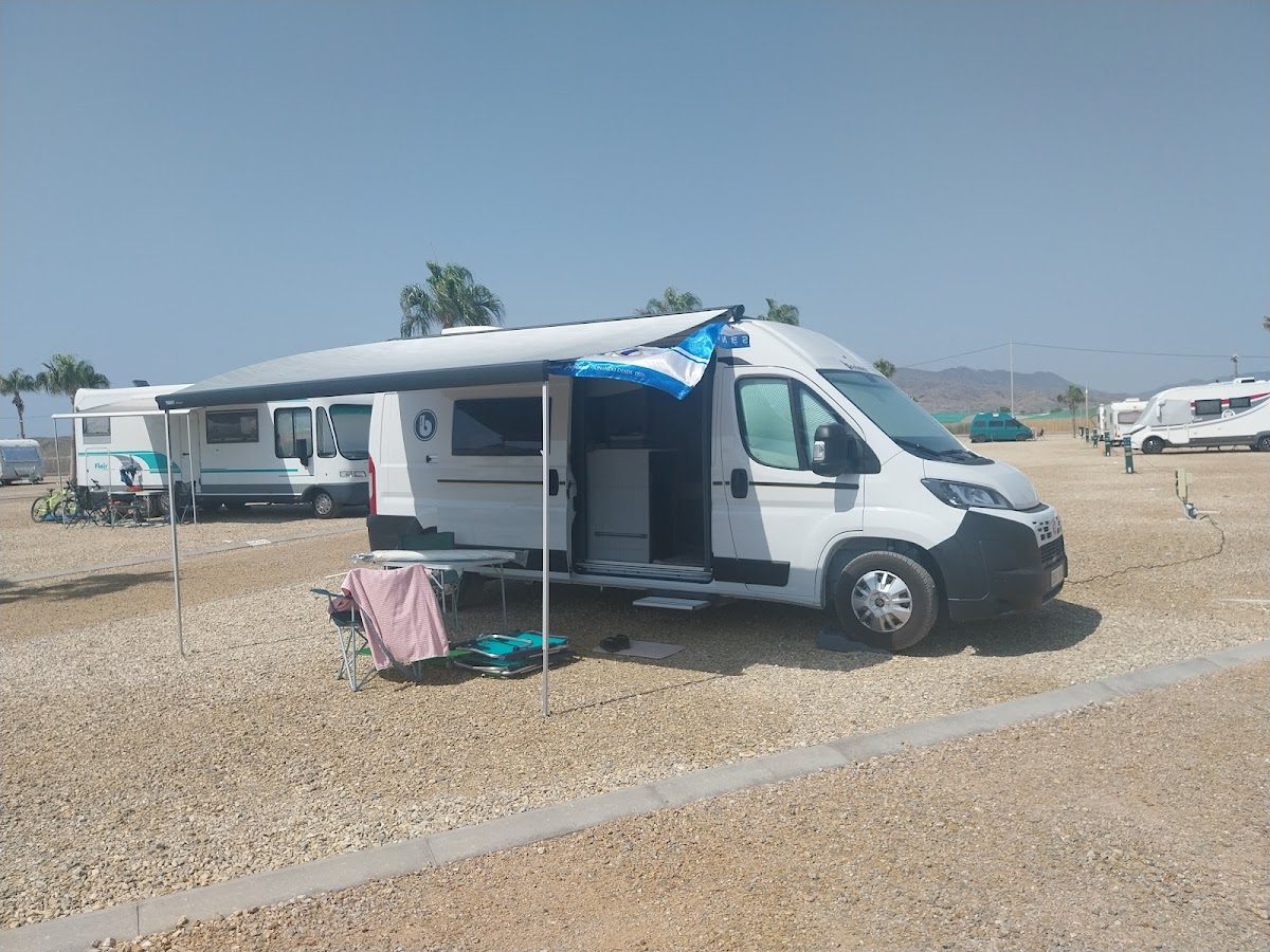 Alemar Alquiler de Camper Van offers a camper van parked at a campsite with an awning and outdoor setup.