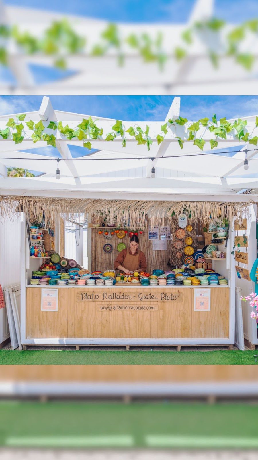 Un animado puesto de mercado en Alfar Tierra Cocida exhibe colorida cerámica y productos artesanales.