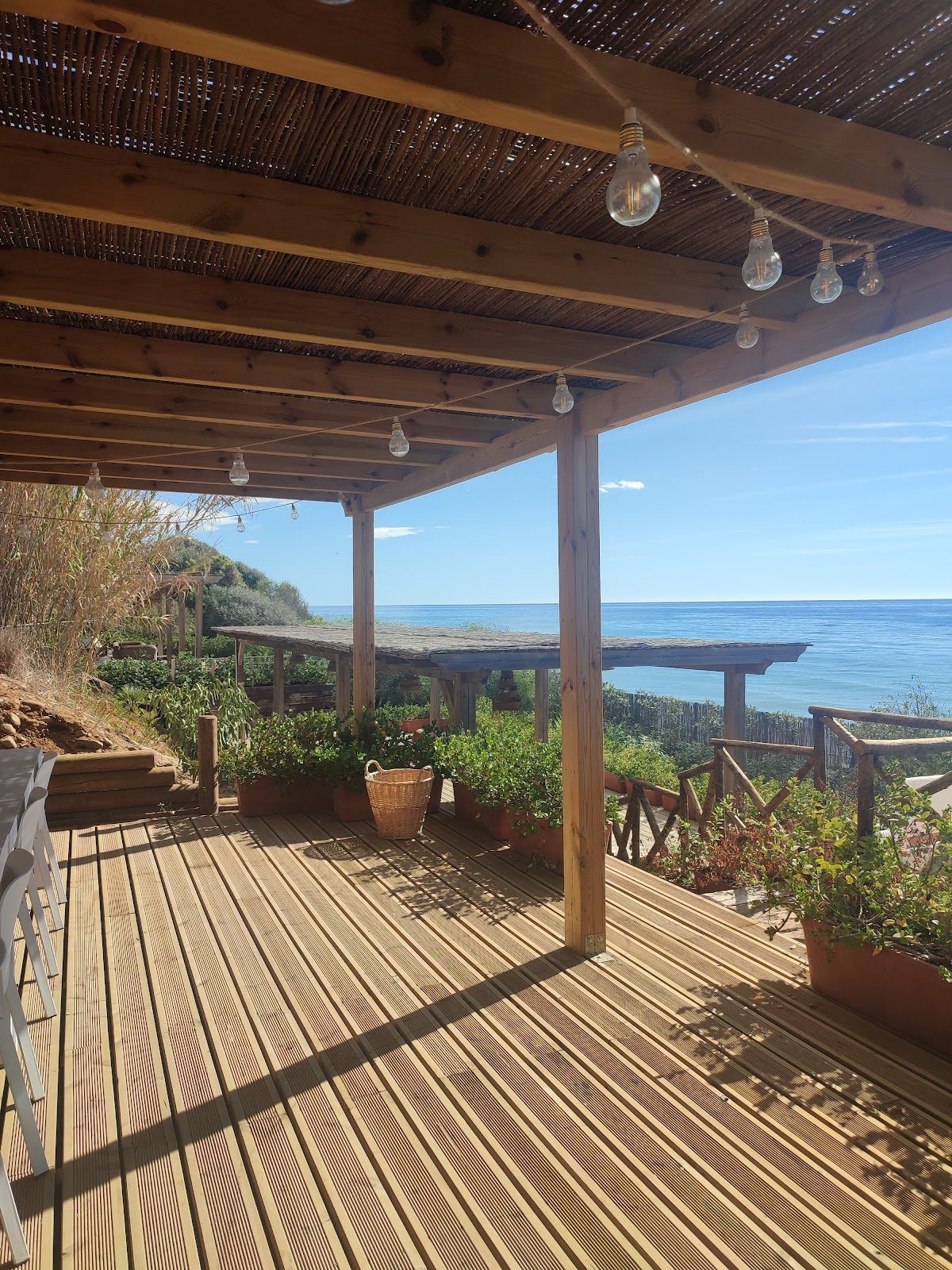 Una terraza de madera con plantas en macetas y vistas al océano, con luces colgantes en Alfombra Roja Marbella.