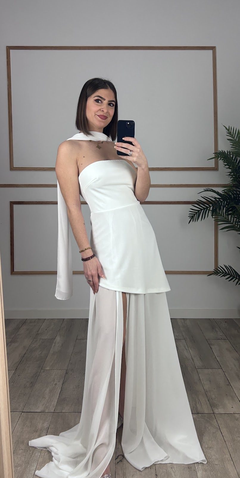 A model showcases a white dress with a flowing design in a stylish fitting room at Alma Modas.