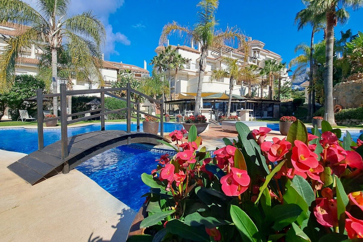 Aloha Hill Club Marbella features a pool surrounded by lush greenery and vibrant flowers.