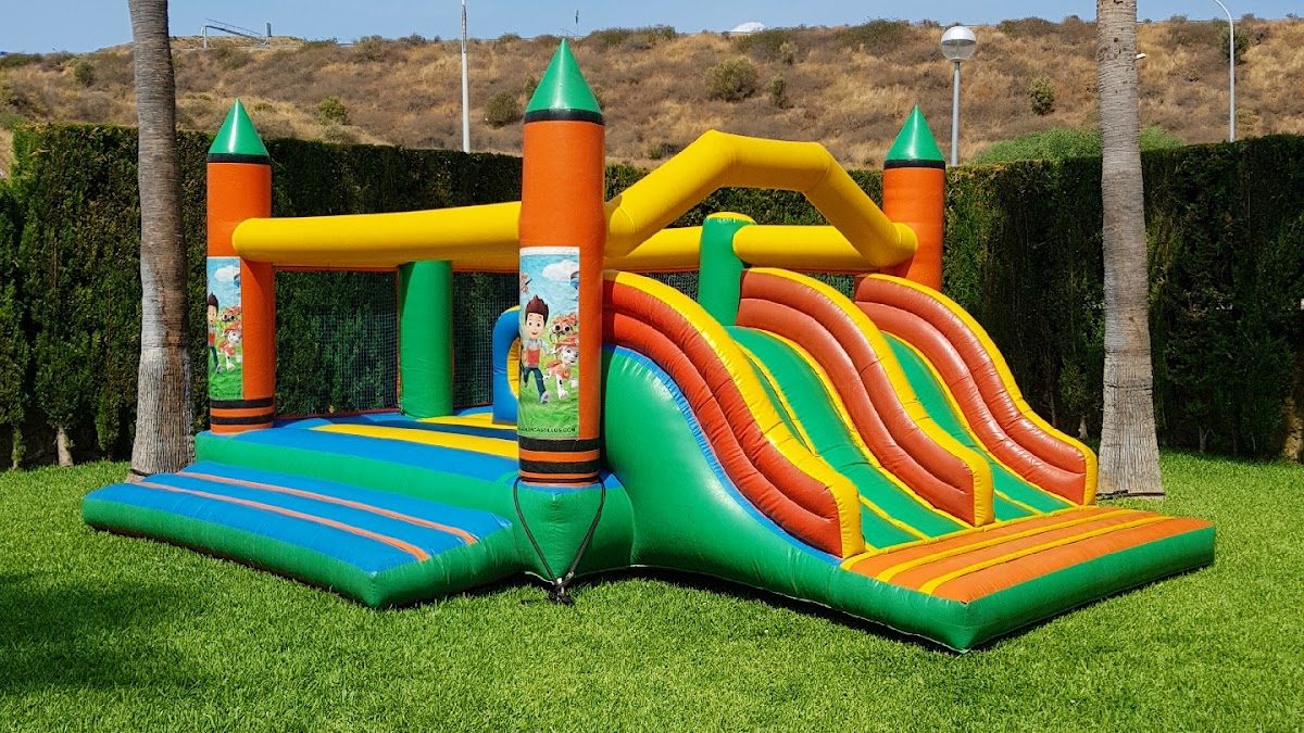 Un colorido castillo hinchable con toboganes, situado sobre césped verde.