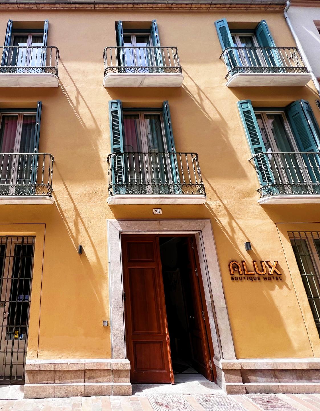 El exterior del Alux Boutique Hotel presenta una fachada amarilla con contraventanas verdes y una entrada acogedora.