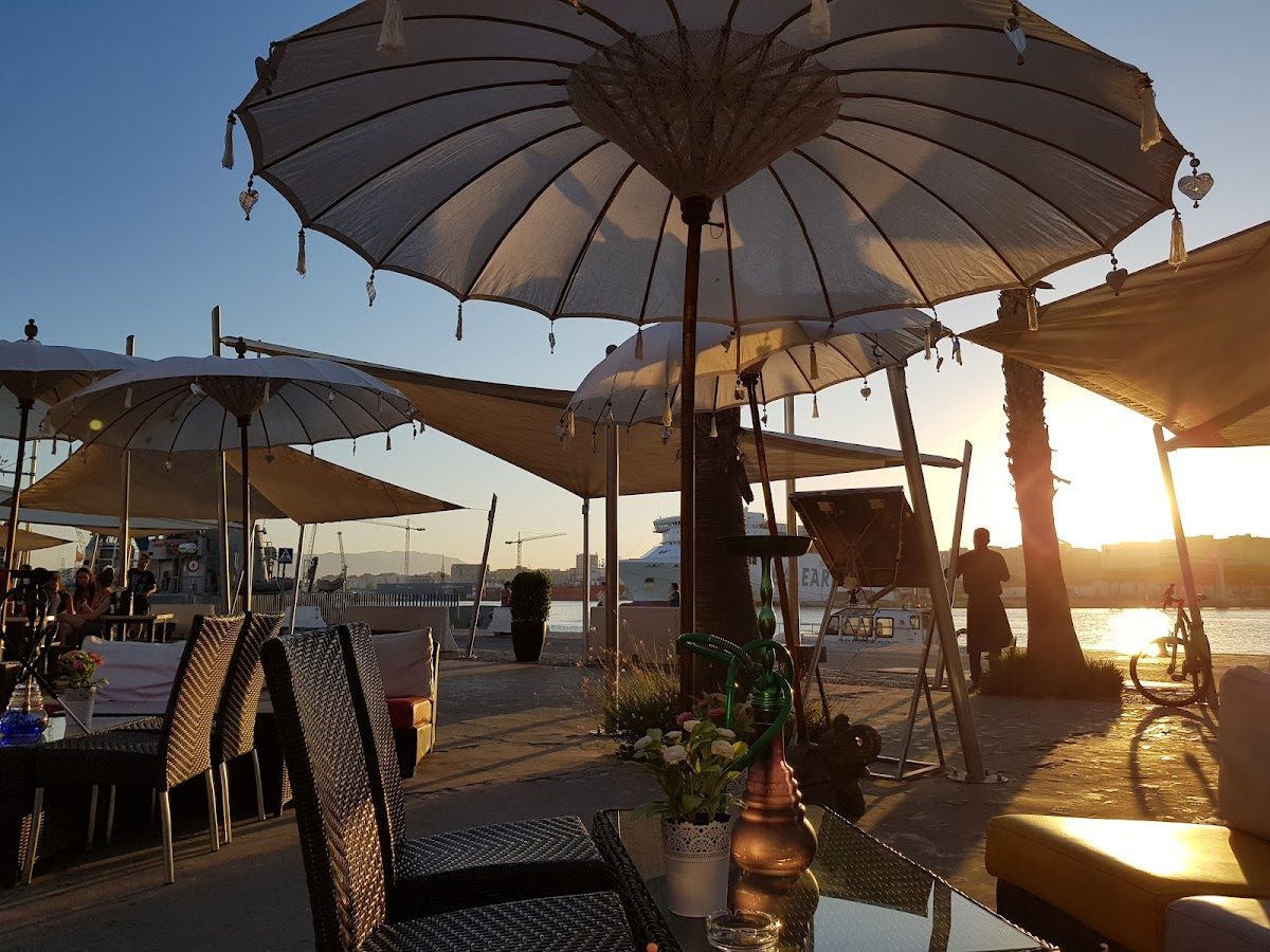 Zona de estar al aire libre en Amigos Muelle Uno con sombrillas, con vistas al paseo marítimo al atardecer.