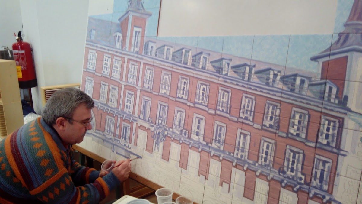 Un hombre pinta un gran mural de cerámica que representa un edificio en Angulo Ceramic Art, en Mijas.