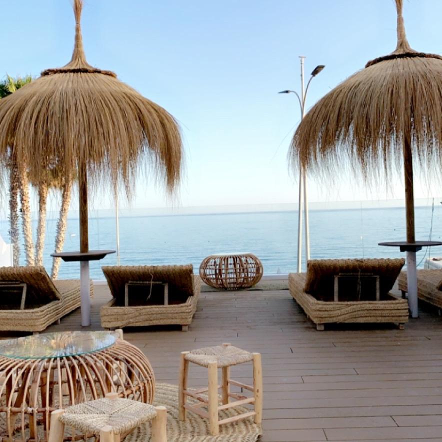 Zona de descanso con sombrillas de paja y tumbonas con vistas al mar en el Apart Málaga.