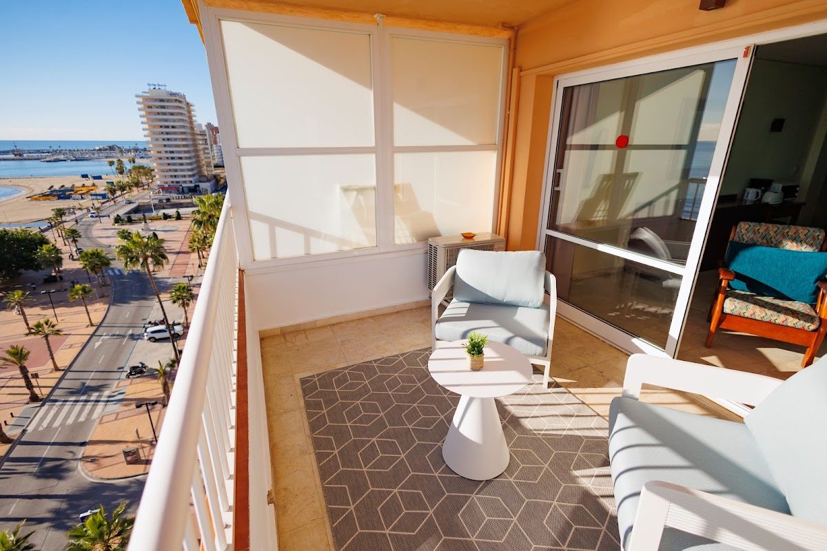 Balcony view from Apartamentos La Jabega, featuring seating and a scenic view of the beach and palm trees.