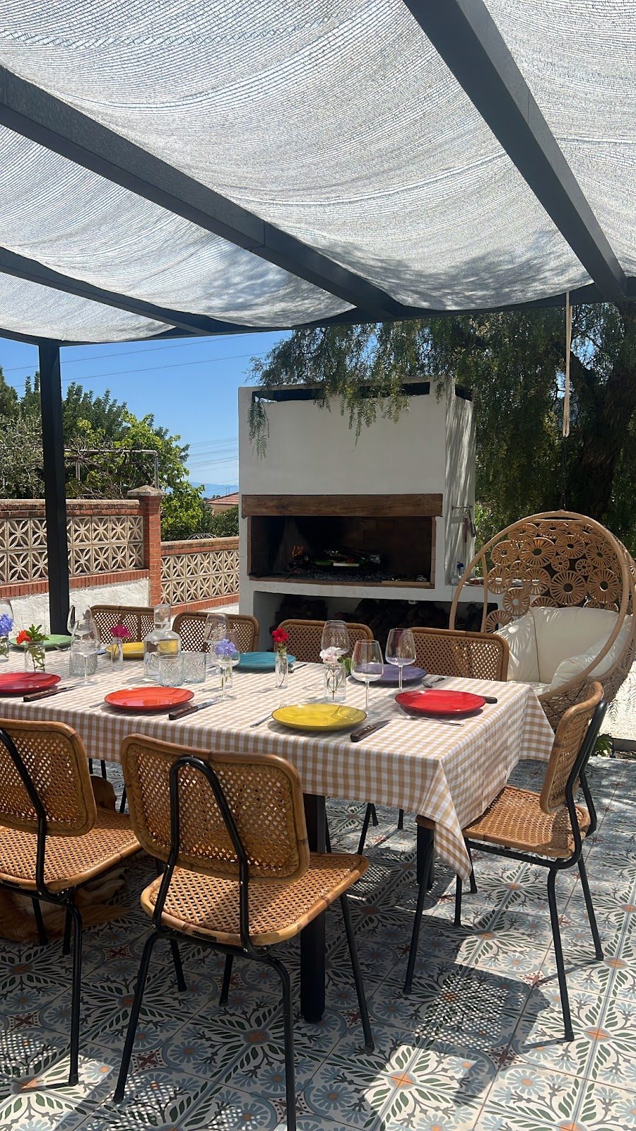 Zona de comedor al aire libre con mantel a cuadros, sillas y parrilla en Argentinian BBQ Experience.