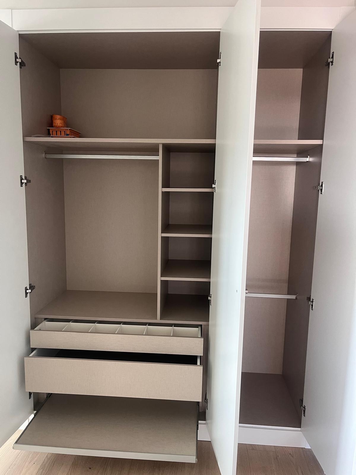 An open wardrobe with shelves and a pull-out drawer, featuring a neutral color scheme.