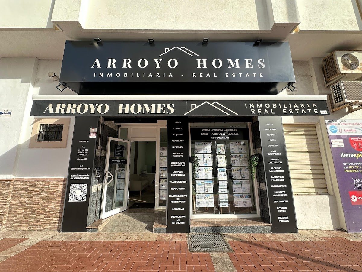 The exterior of Arroyo Homes Inmobiliaria features a modern black facade with large signage and property listings displayed.