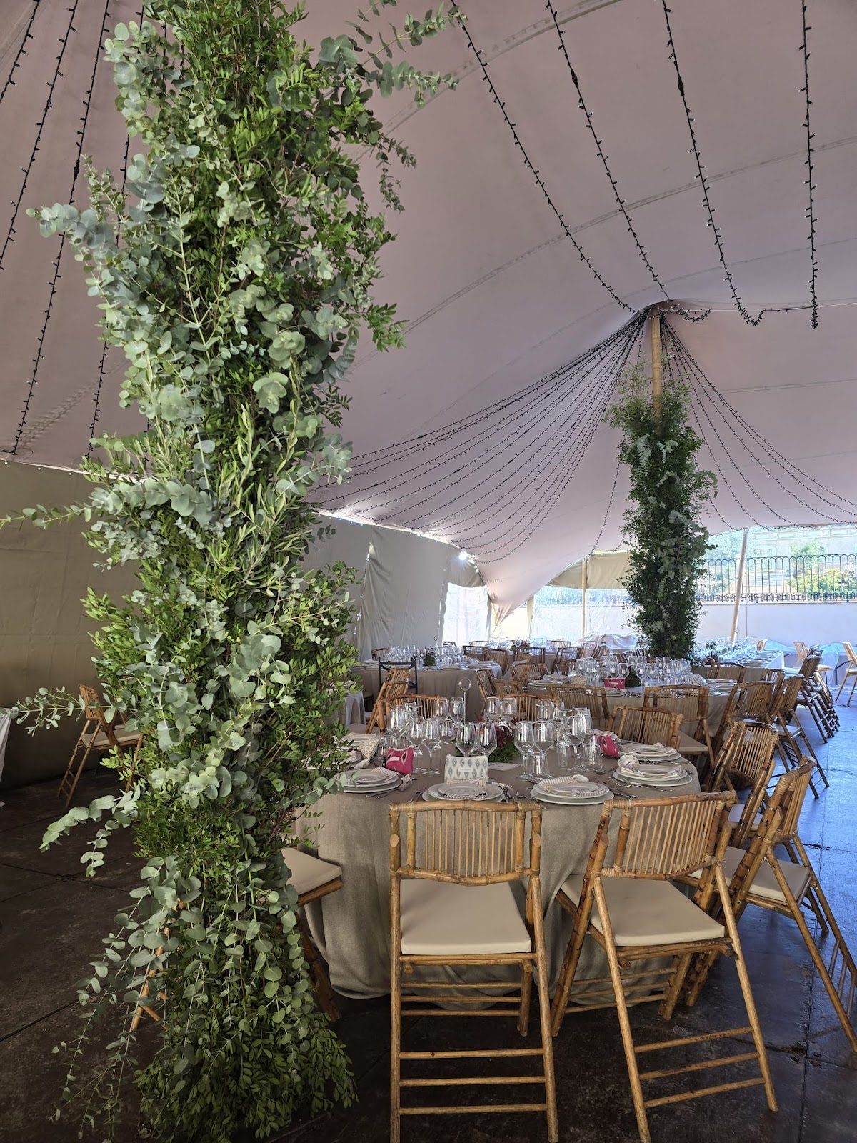 Un espacio para eventos bellamente decorado con altos arreglos de vegetación y elegantes mesas puestas.