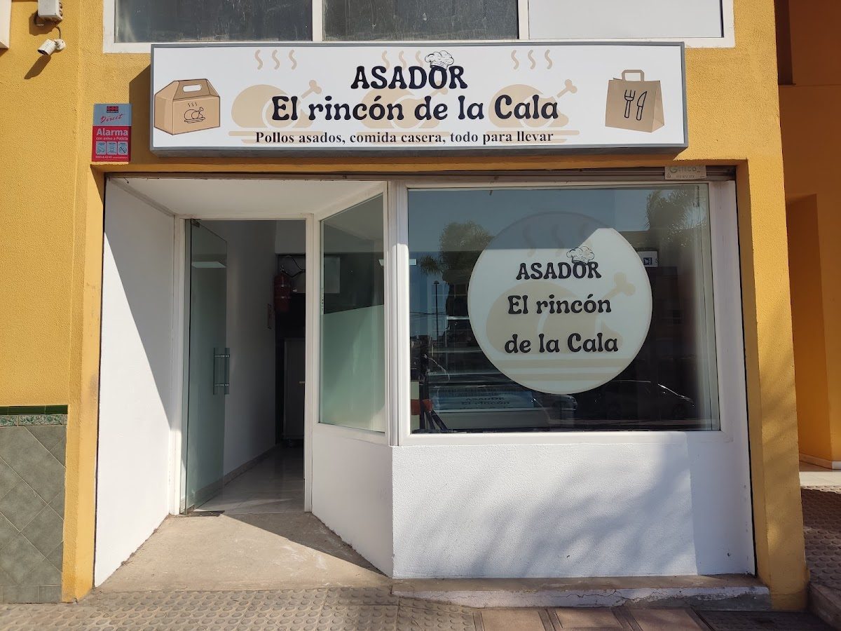 Vista exterior del Asador El Rincón de la Cala, con un gran letrero y una ventana de cristal.