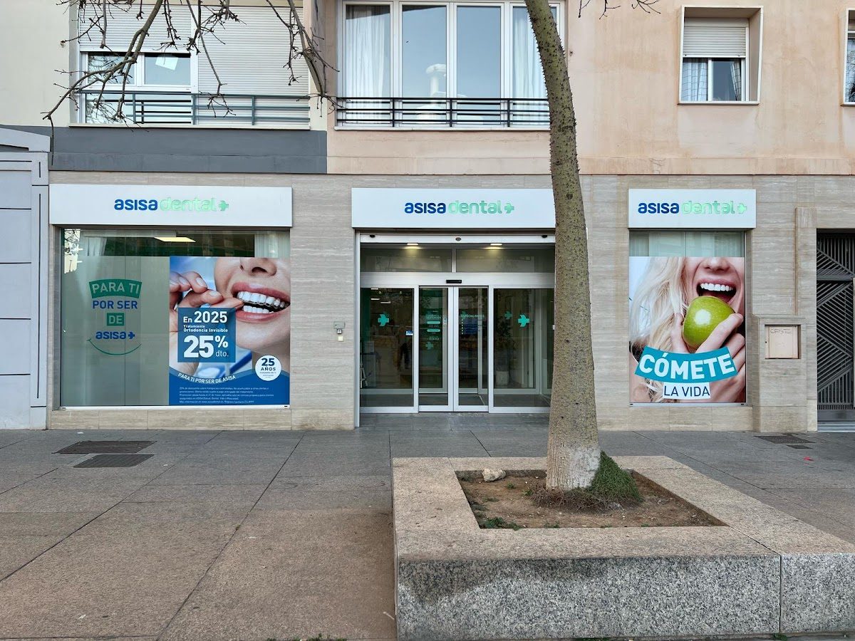 La clínica dental Asisa presenta un exterior moderno con grandes ventanales que muestran imágenes promocionales y letreros.