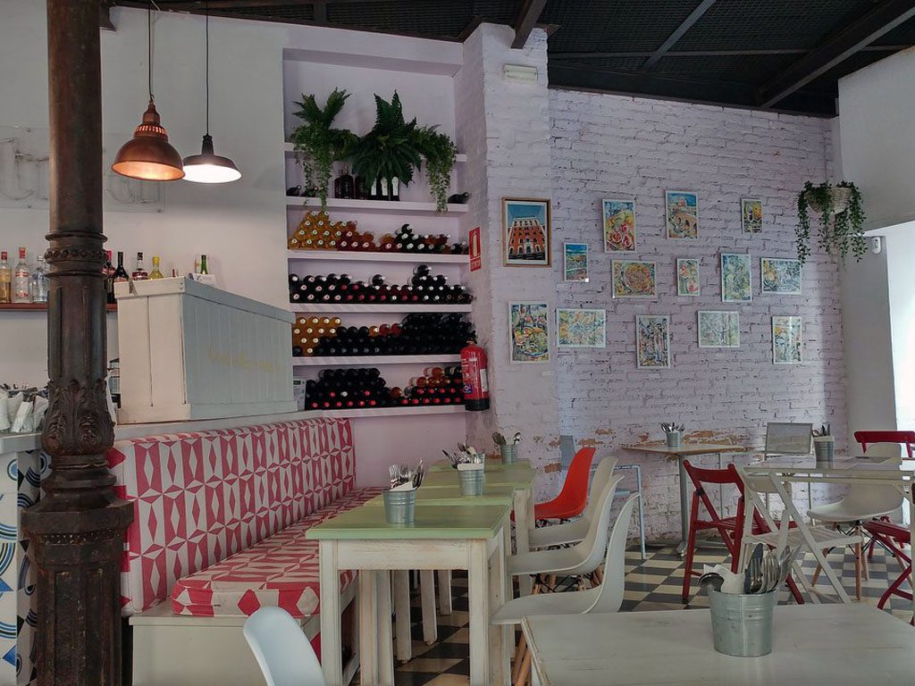 Interior de Astrid: Tapería orgánica con asientos coloridos, estantes para vinos y arte decorativo en las paredes.