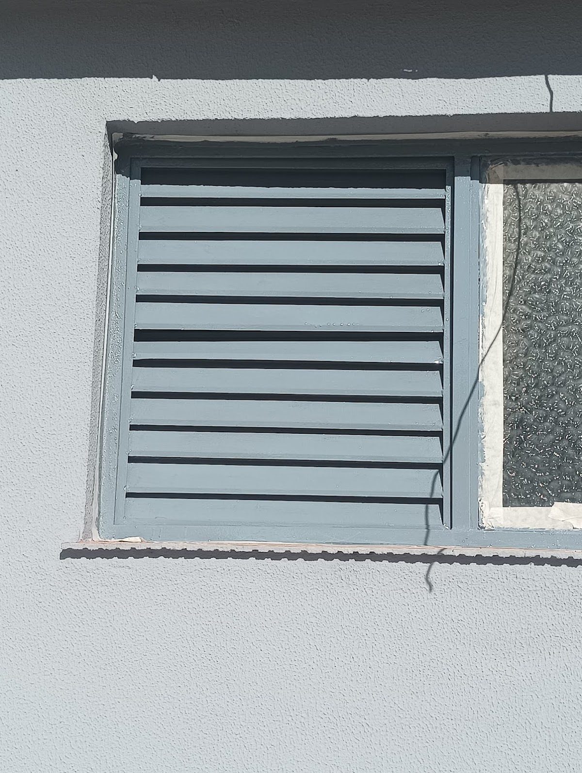 Una ventana con contraventanas azules en una pared exterior gris, posiblemente de un edificio en Málaga.
