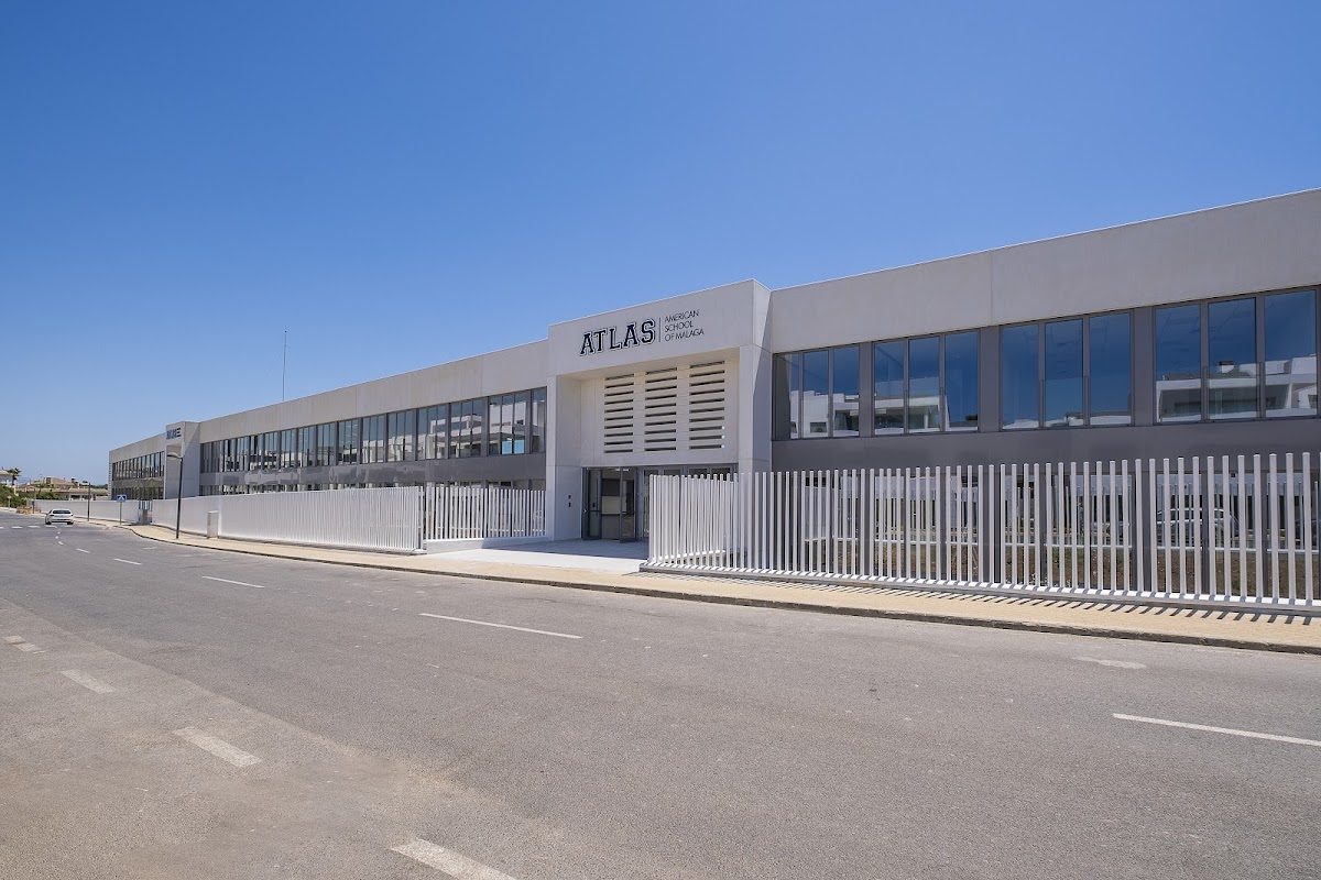Modern building of Atlas American School of Malaga with large windows and a white fence along the road.
