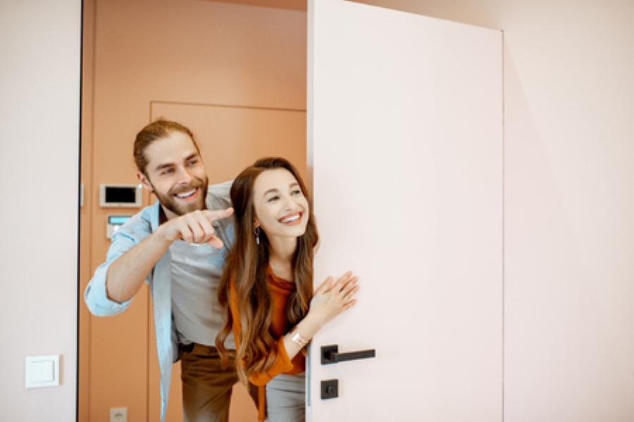 Una pareja sonriente se asoma por una puerta rosa, mostrando un ambiente acogedor en AYRE ESTATES.