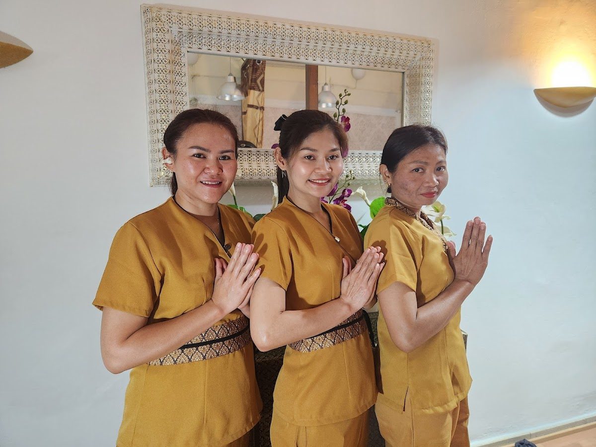Tres miembros del personal, vestidos con atuendos tradicionales tailandeses, posan con las manos juntas en un gesto de bienvenida en Bangkok Thai Massage.
