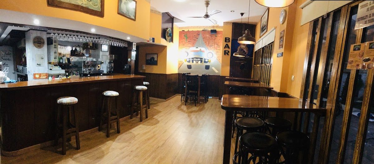 Interior view of Bar Chevrolet featuring wooden bar stools, a counter, and warm orange walls.
