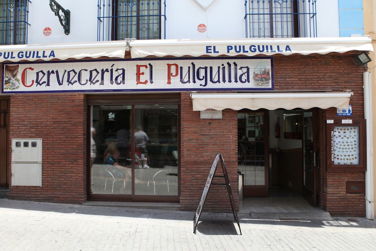 The exterior of Bar El Pulguilla features a brick facade with a sign displaying its name and a menu board outside.