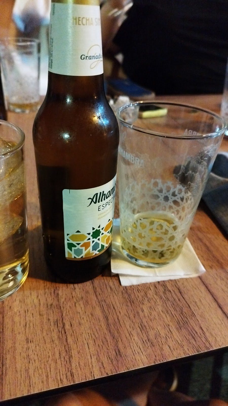 Una botella de cerveza Alhambra junto a un vaso sobre una mesa de madera en el Bar La Caña.