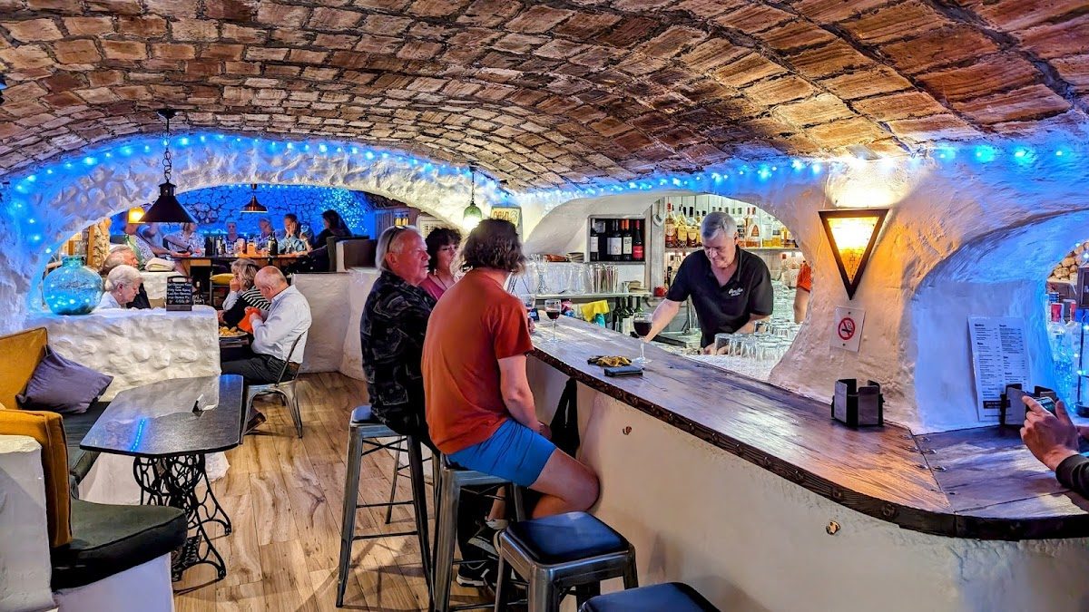 Bar La Cueva features a cozy, arched interior with blue lighting and patrons seated at the bar.