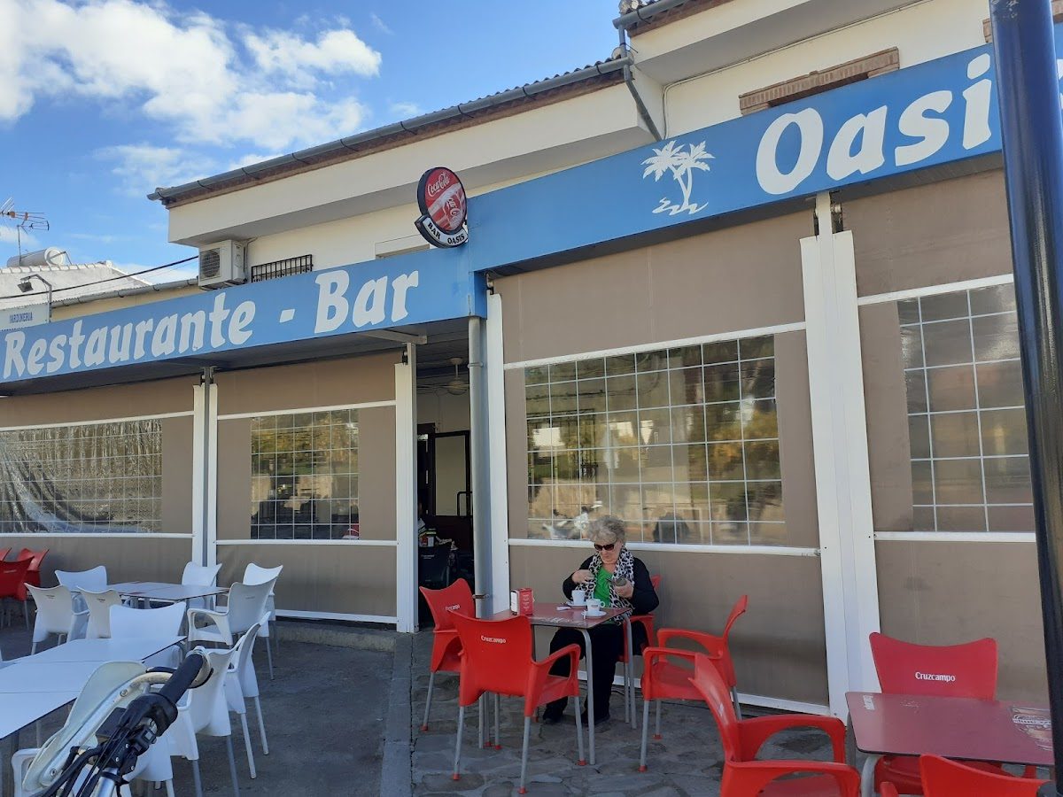 El Bar Oasis, ubicado en Villanueva de la Concepción, cuenta con una terraza con sillas rojas y un gran letrero.