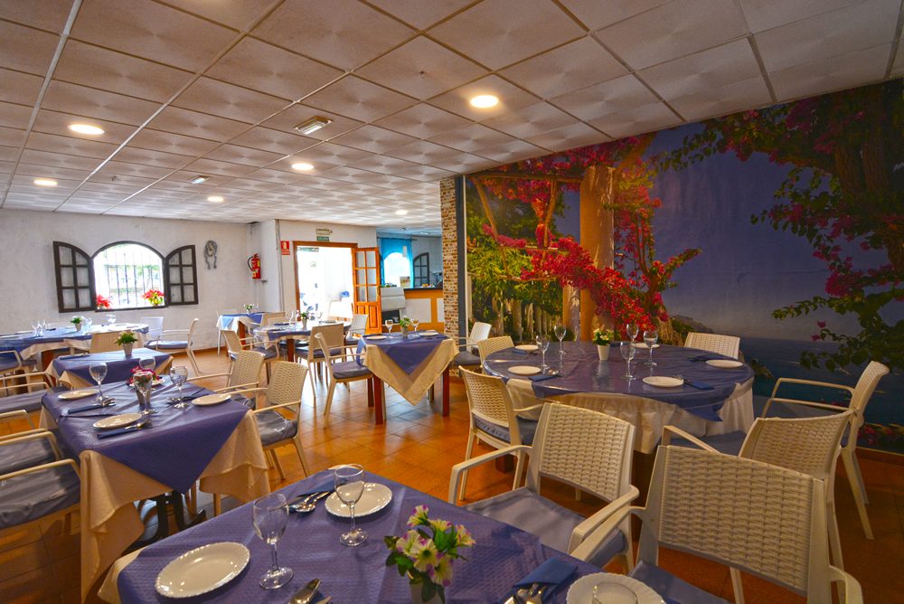 Interior of Bar Restaurante Sabor Andaluz Coín featuring tables with blue tablecloths and a vibrant mural.