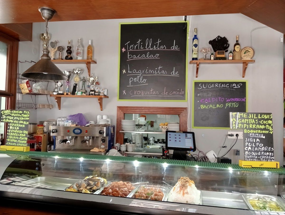 El Bar Zea cuenta con una animada zona de bar con estanterías repletas de bebidas, una exposición de comida y una pizarra con el menú.