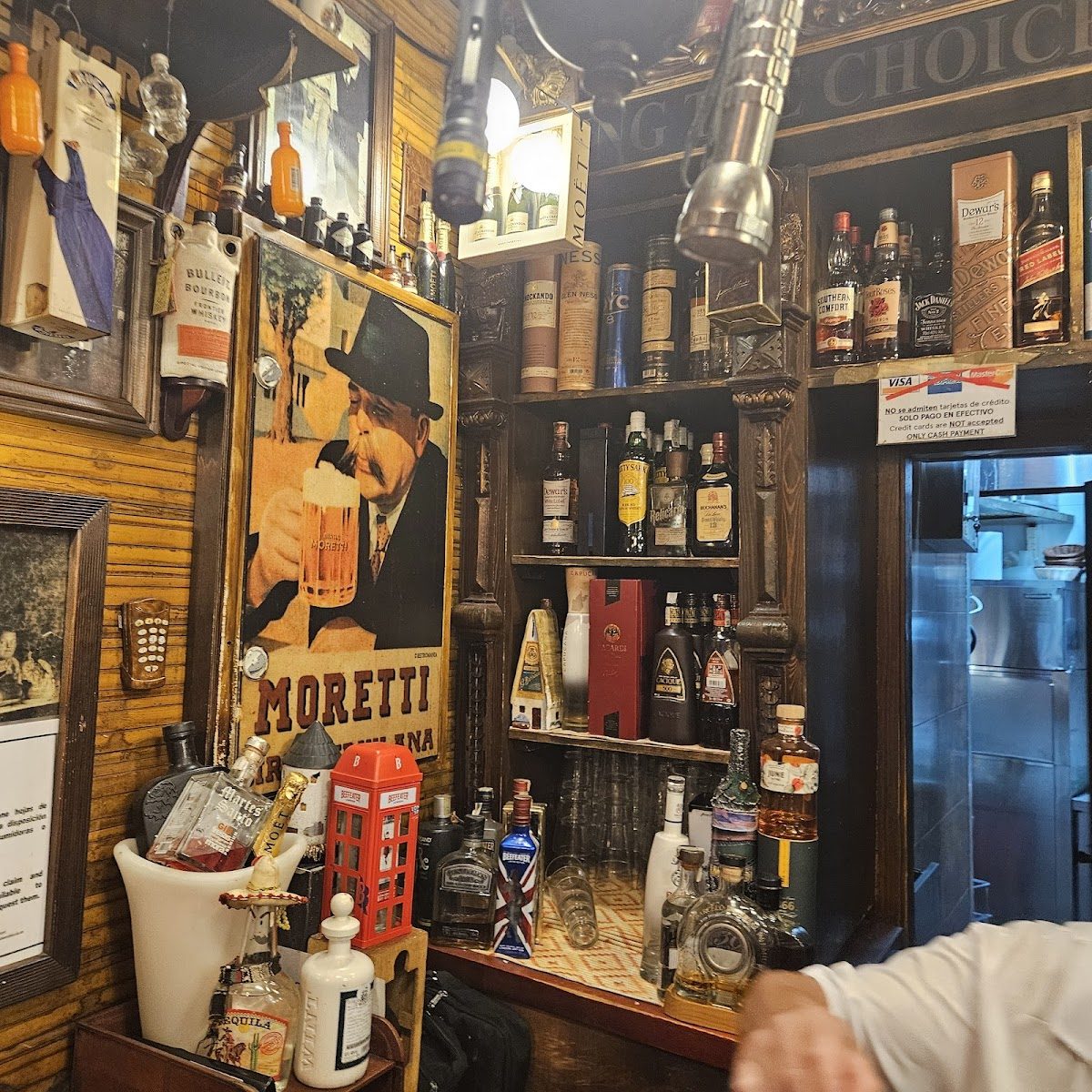 El interior del restaurante Be Happy cuenta con una barra de madera con varias botellas y un letrero de cerveza antiguo.