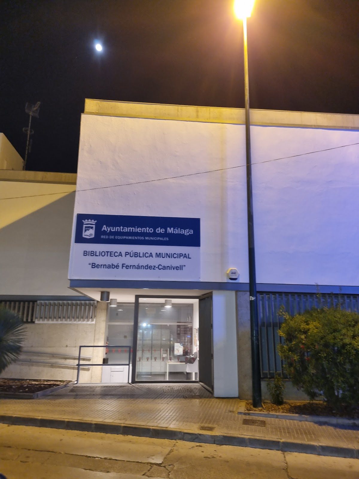 The entrance of Bernabé Fernández-Canivell library, featuring a sign and illuminated at night.
