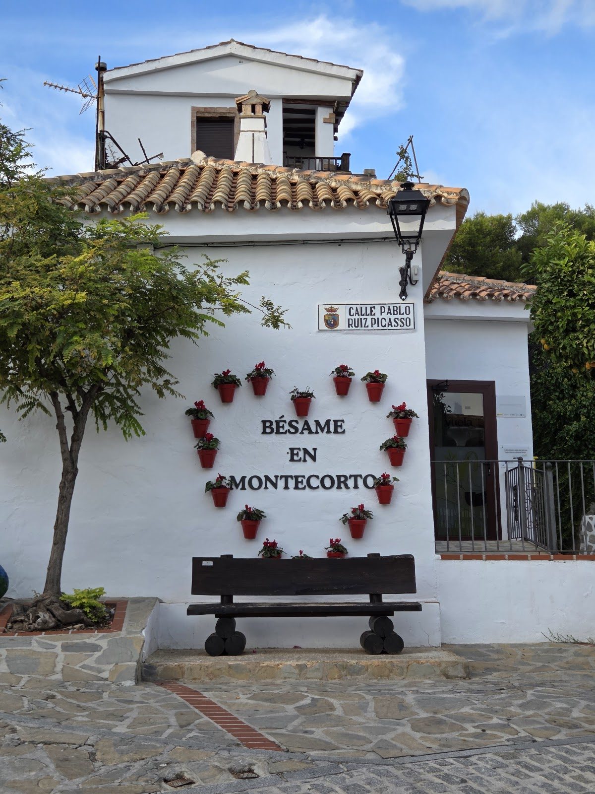 Un encantador edificio blanco con una composición de macetas en forma de corazón y un banco de madera en el exterior.
